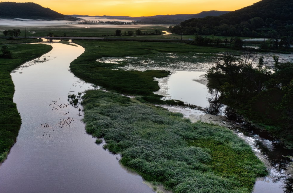 Image of river running through a valley of green grass at sunset.